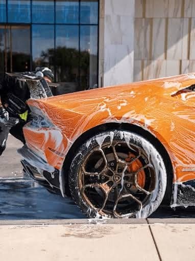 Orange supercar covered in wash foam during an exterior detail
