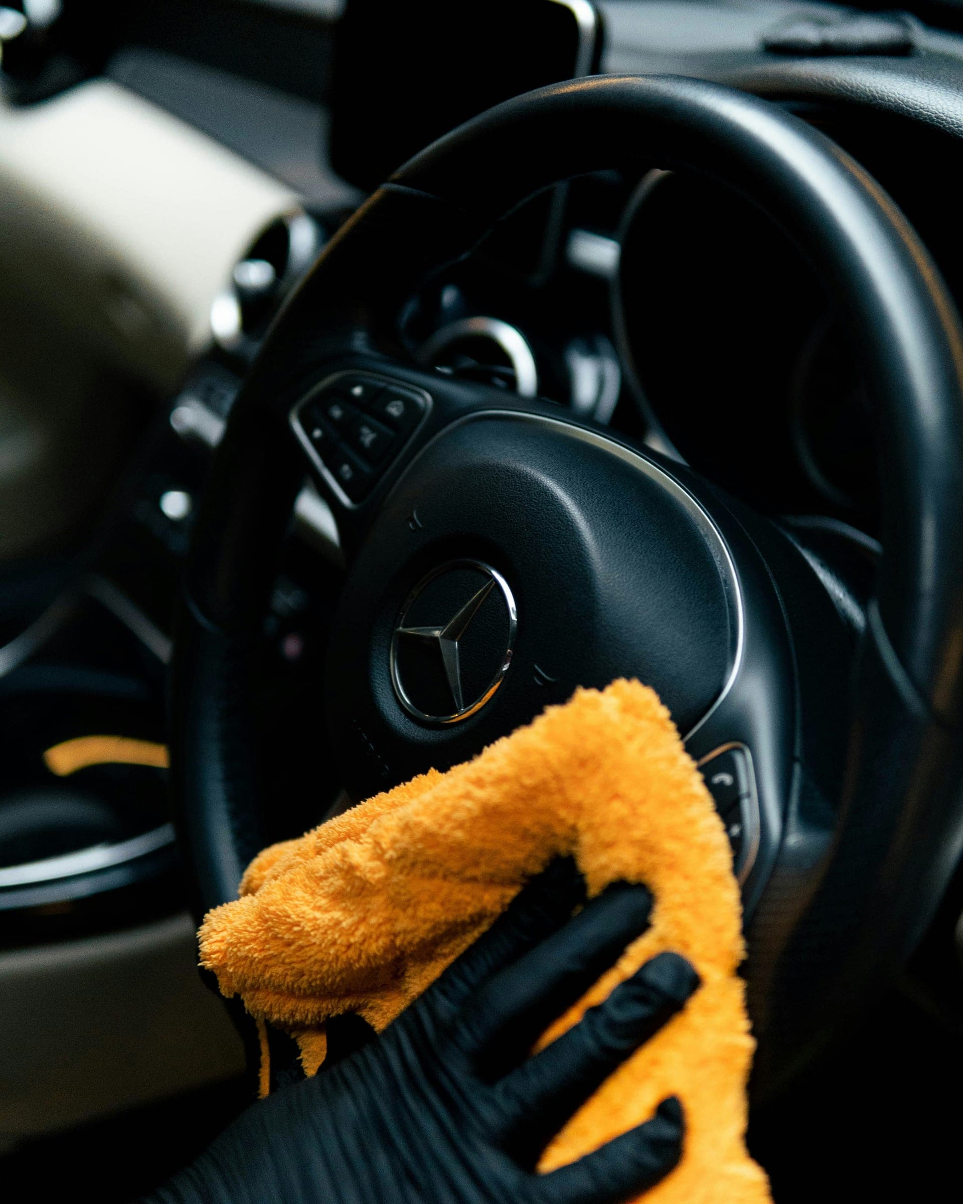 Gloved detailer wiping down a Mercedes steering wheel with a microfiber towel