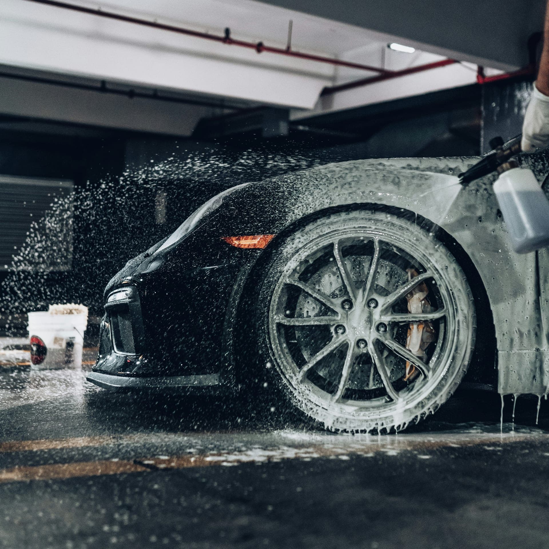 Low-angle view of a black Porsche wheel being rinsed during a wash